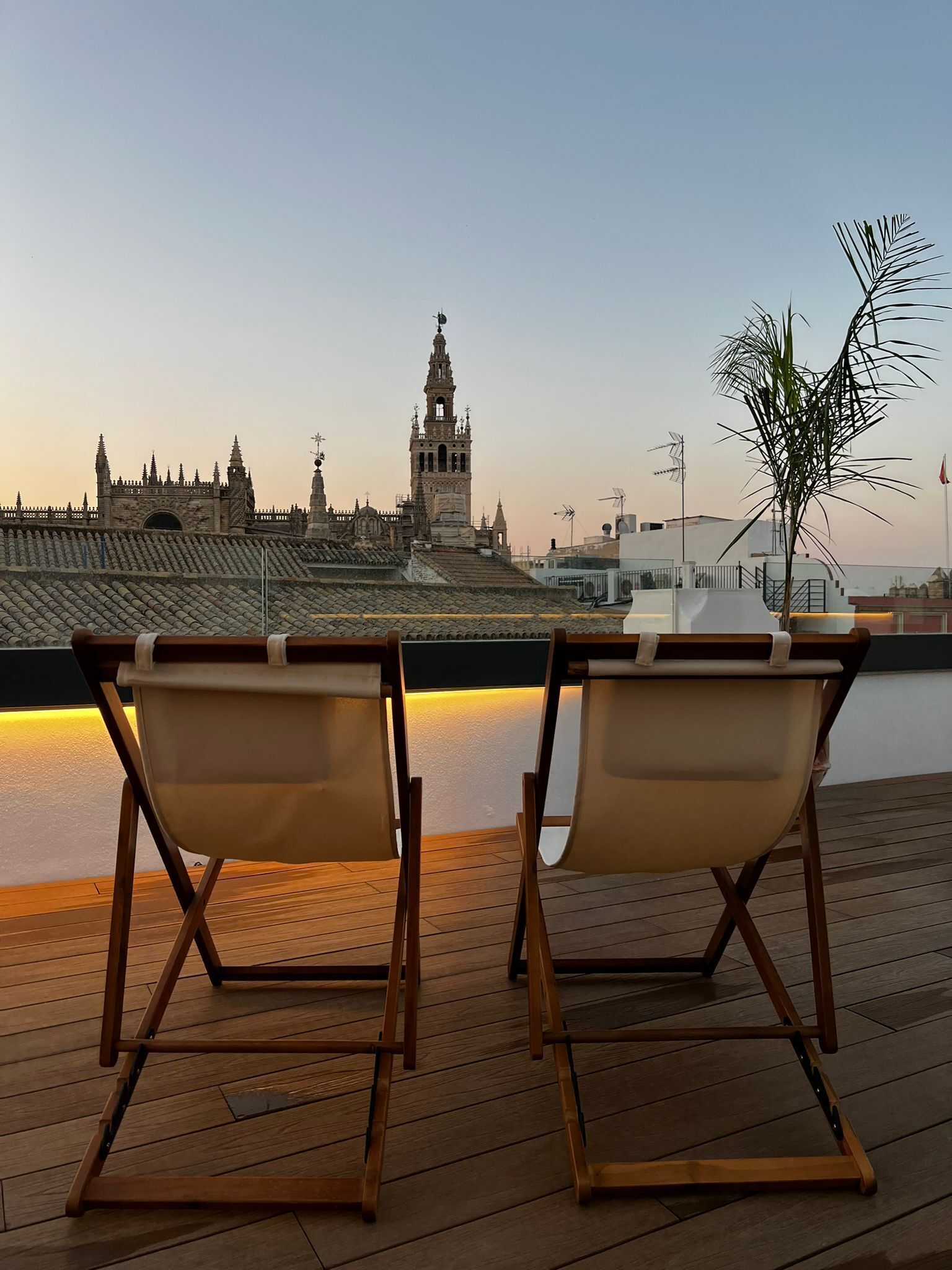 Two wooden lounge chairs facing a waterfront with a historic building in the background.