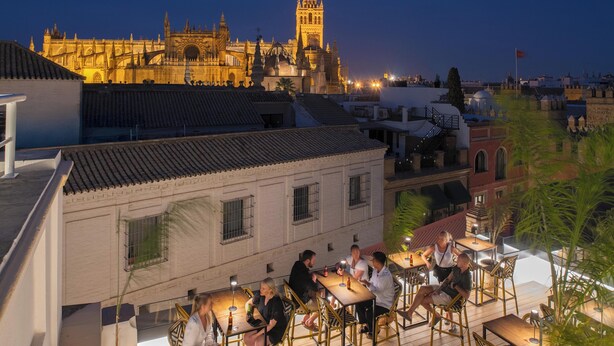 Un bar en la azotea con mesas al aire libre y vistas a un edificio histórico con una torre destacada.