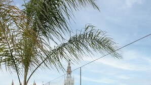 Zona de piscina con mobiliario de madera, dos lámparas y vistas a edificios históricos.
