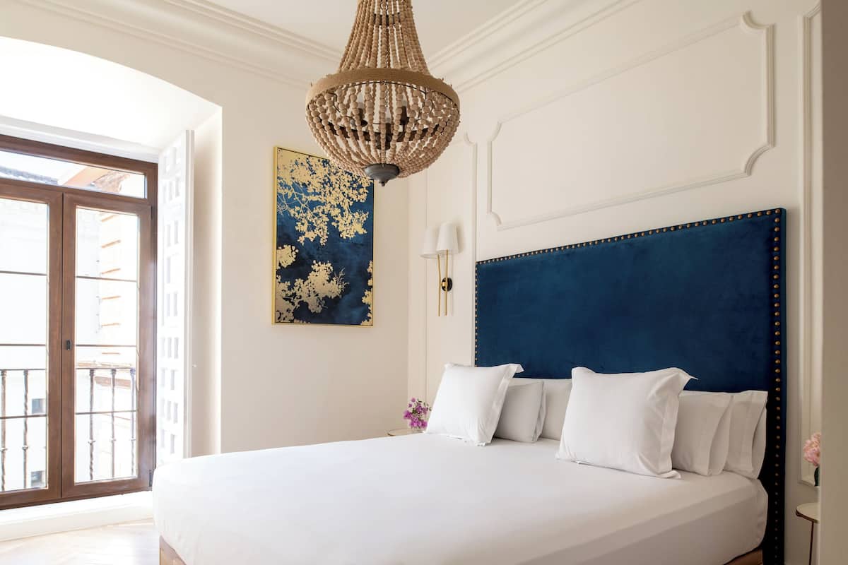 A large bed with a dark headboard, white bedding, and a chandelier above.