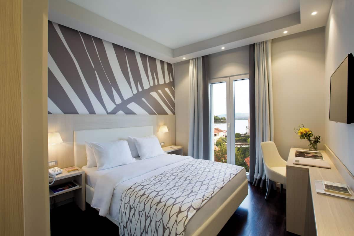 A hotel room with a large bed, a desk, a chair, a TV, and a window with a view.