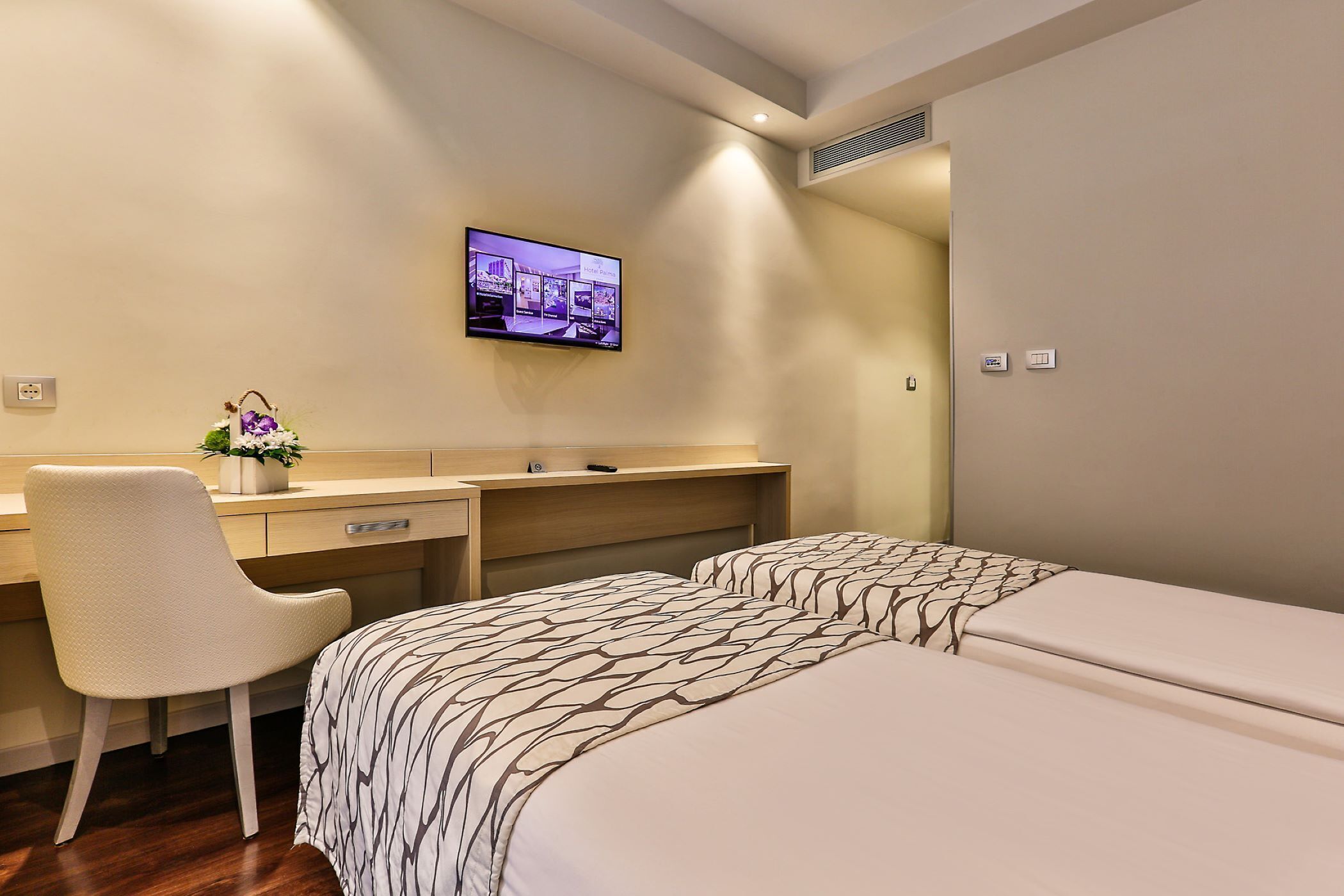 A hotel room with a bed, a desk, and a TV mounted on the wall.