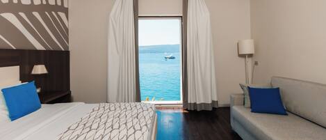 Habitación de hotel con cama, sofá, vista al mar y ventana con cortinas.