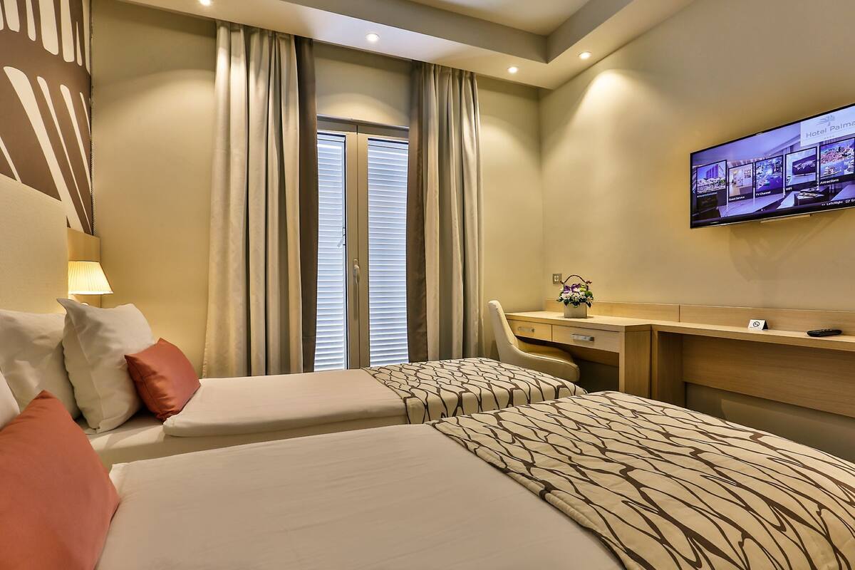 A hotel room with two beds, a desk, a chair, a television, and a window with curtains.