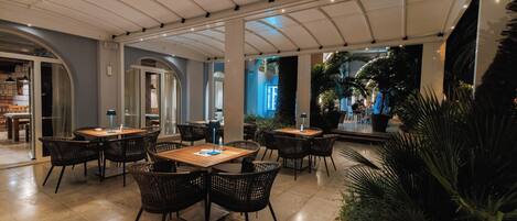 Un comedor interior con mesas y sillas, suelo de baldosas e iluminación empotrada en el techo.