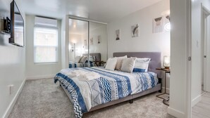 A bedroom with a large bed, a sliding door closet, a mounted TV, and a window with blinds. - A/C, 3 blocks to beach, dogs, shopping, dining (San Diego)