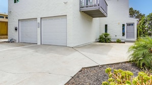 A two-story house with a white exterior, two garage doors, a balcony, and a small garden area with plants. - A/C, 3 blocks to beach, dogs, shopping, dining (San Diego)