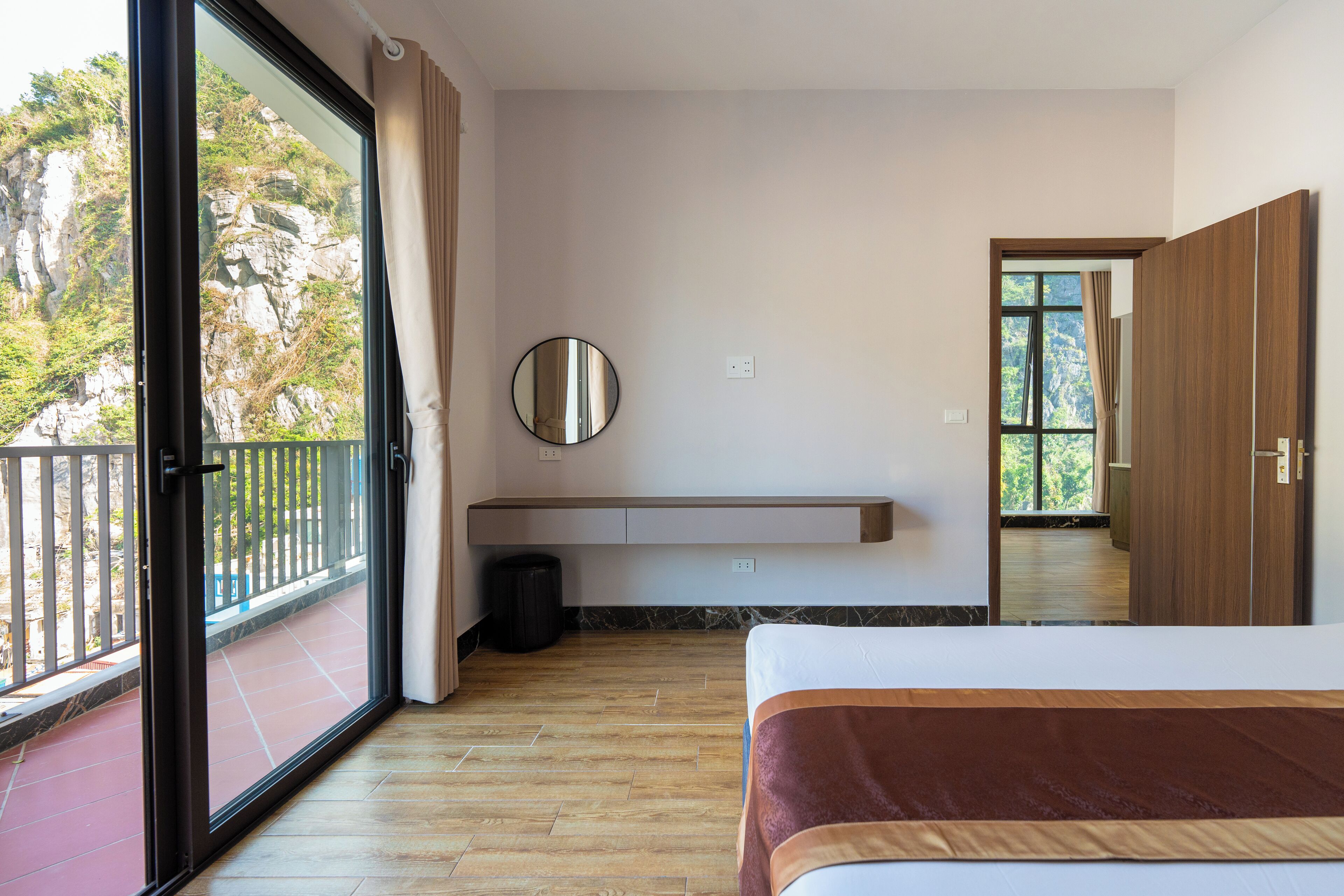 A bedroom with a bed, a bedside table, a mirror, a window, and a balcony.