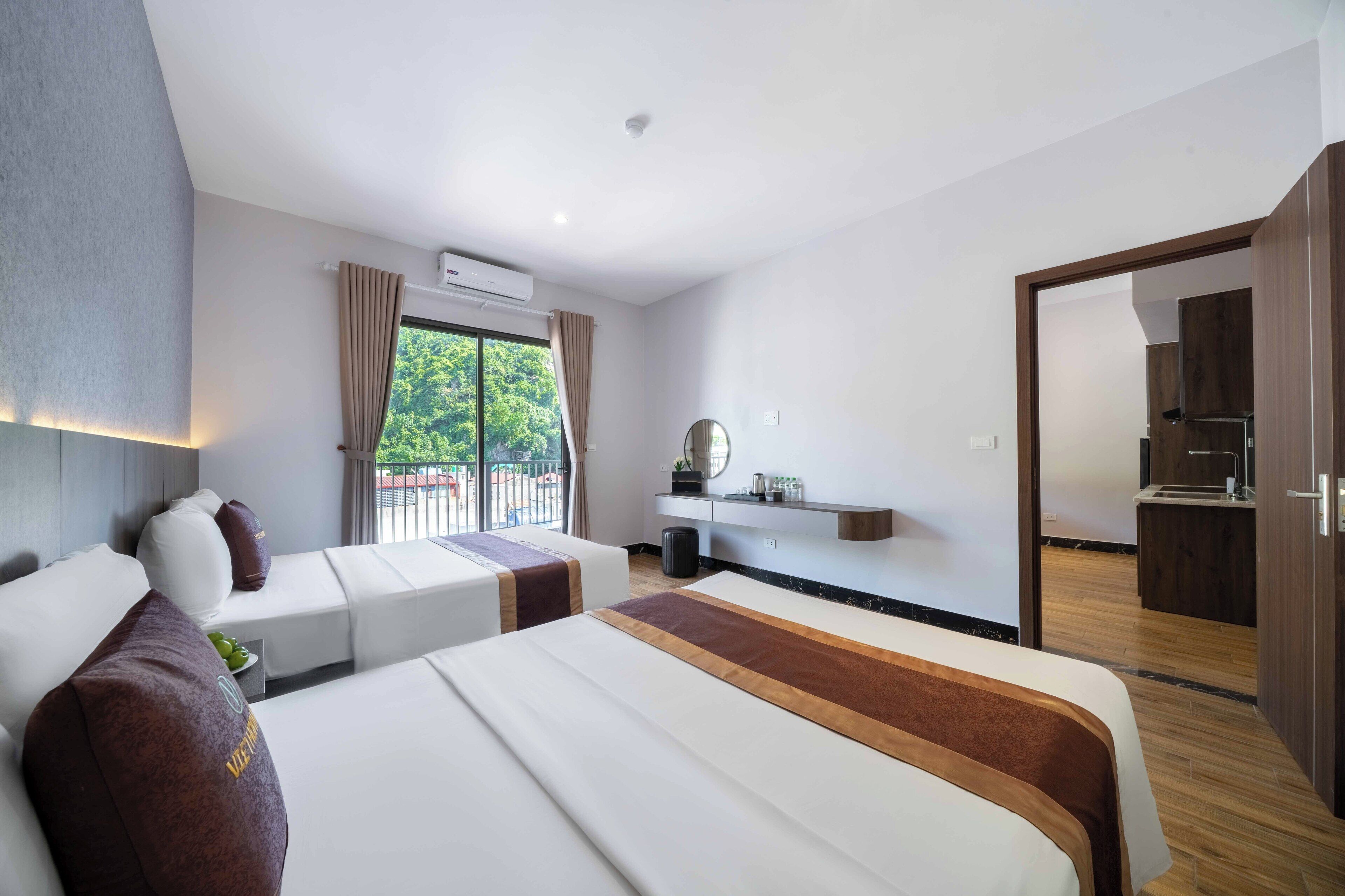 Une chambre d’hôtel moderne avec deux lits, un coin salon, une petite kitchenette et une vue sur l’extérieur.