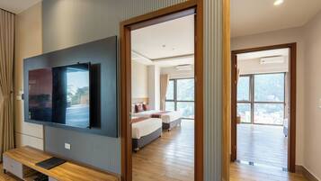 Una habitación de hotel moderna con un televisor de pantalla plana grande, un escritorio de madera, una cama con vistas y un ventanal amplio.