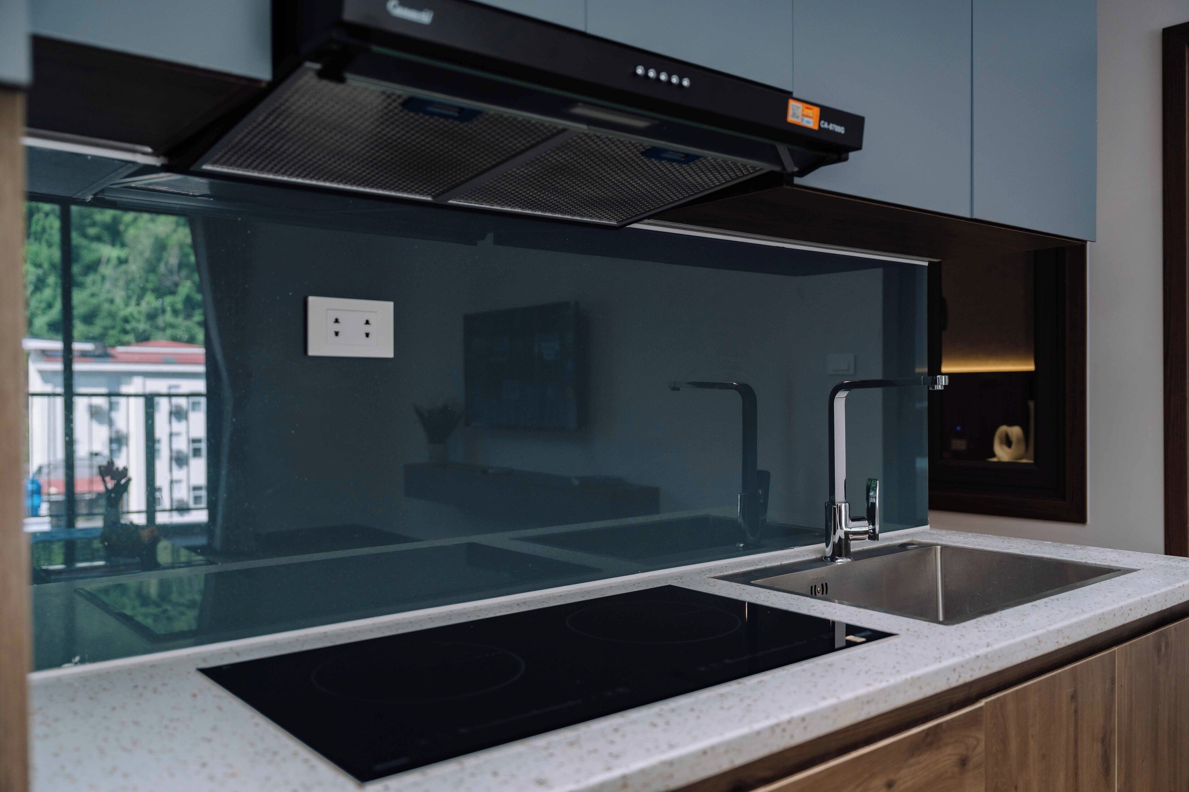A modern kitchen with a black induction cooktop, a stainless steel sink, and a range hood above the cooktop.