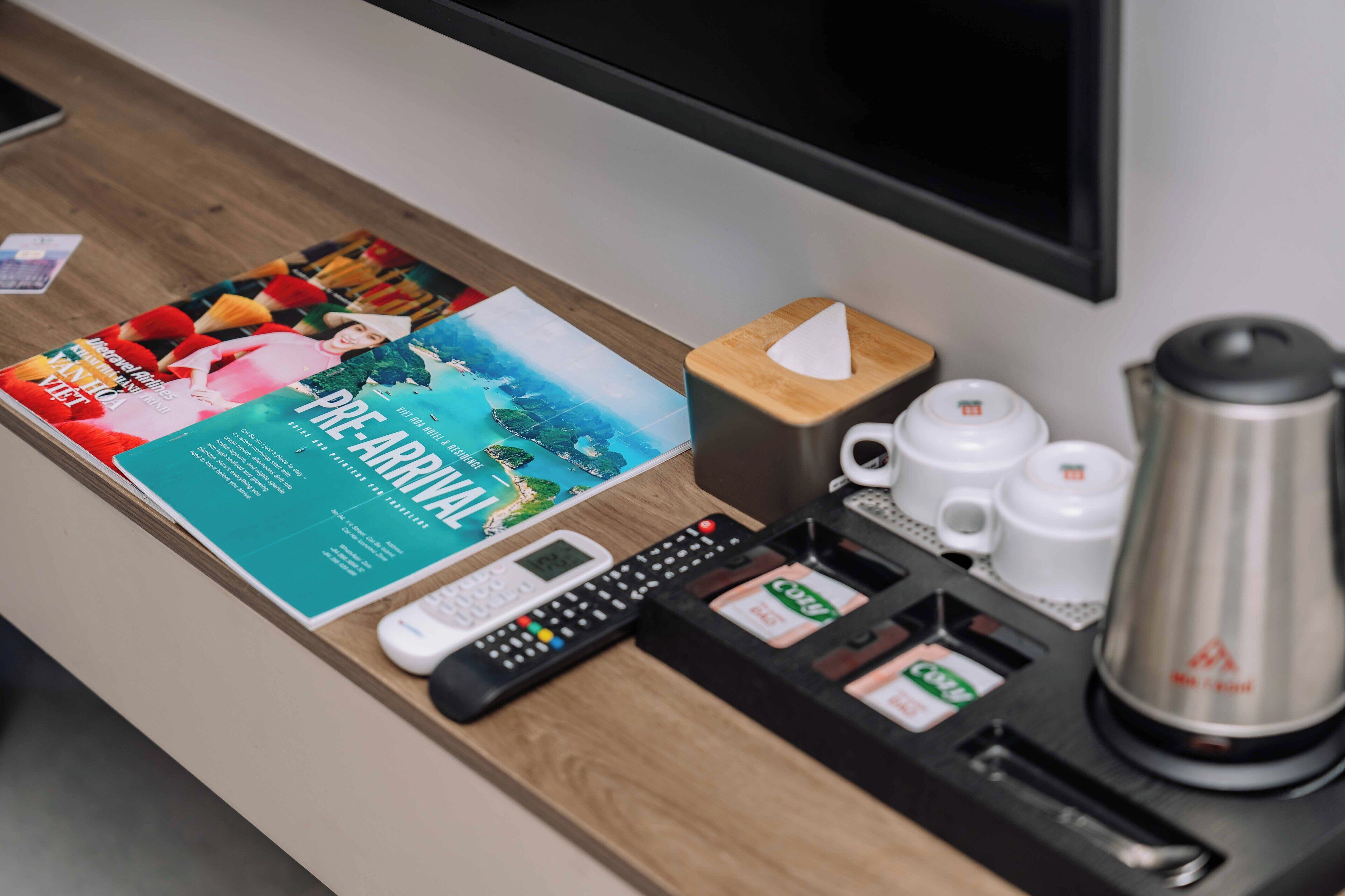 A hotel reception desk with a magazine, a remote control, a coffee maker, and a tea dispenser.