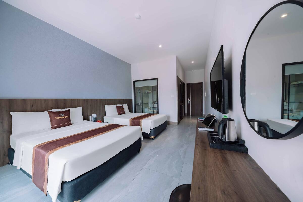 A hotel room with two beds, a large mirror, a TV, and a coffee maker.