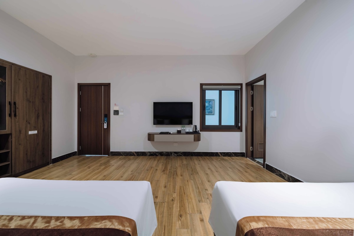 Een hotelkamer met twee bedden, een aan de muur bevestigde televisie en een houten vloer.