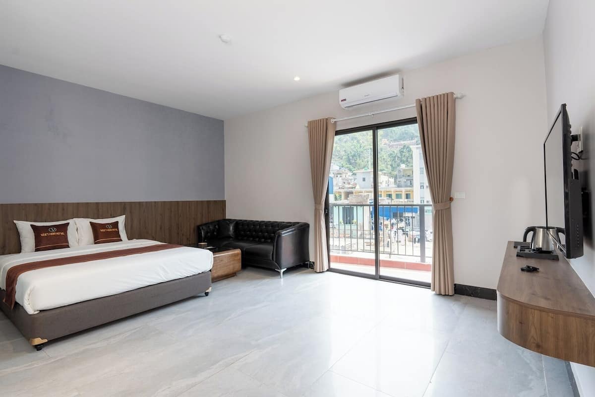 A modern hotel room with a large bed, a sofa, a TV, and a balcony with a view of the city.