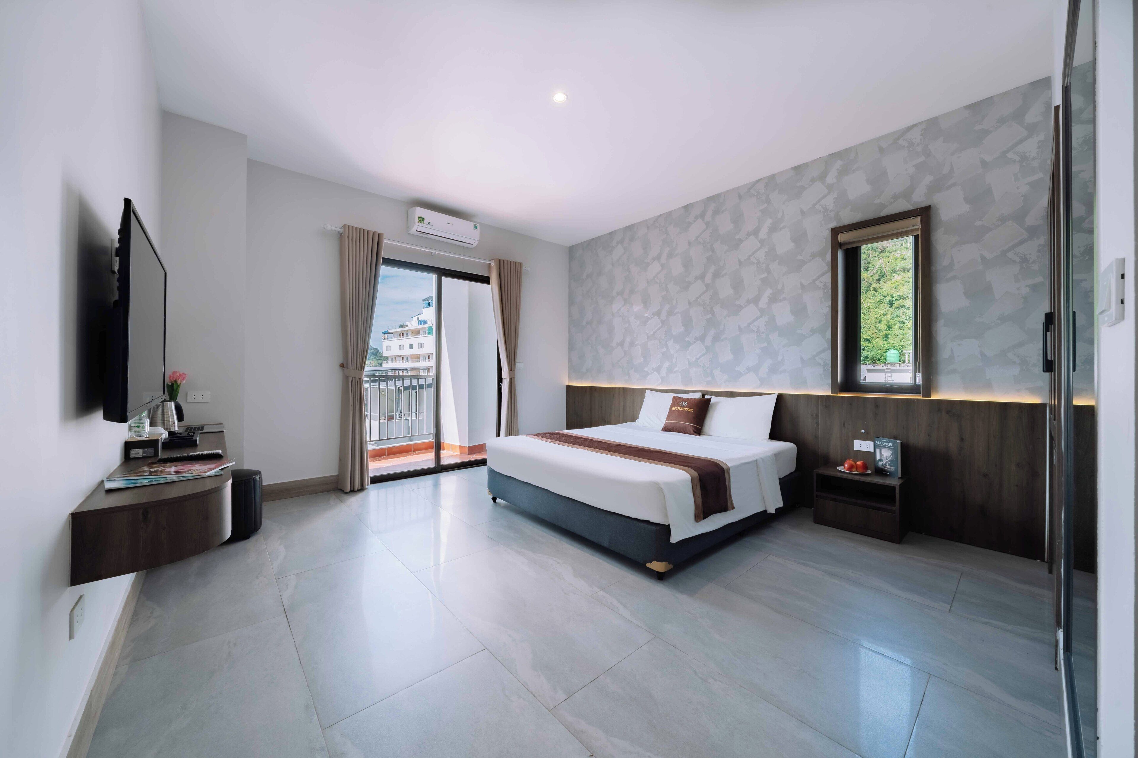 A modern hotel room with a large bed, a TV, a desk, and a balcony with a city view.
