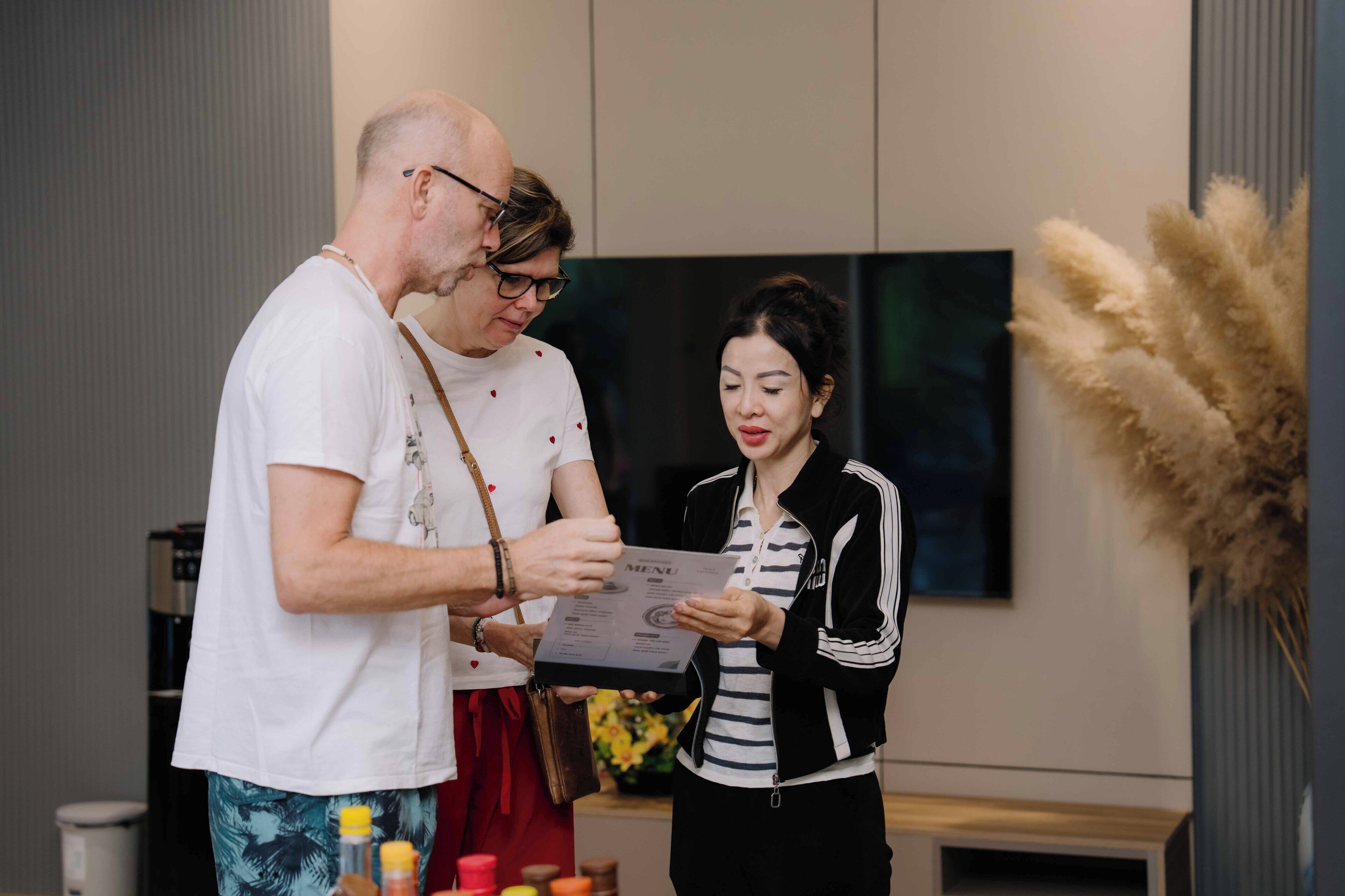 Two people in a modern kitchen with a large flat-screen TV, a coffee machine, and a vase with dried plants.