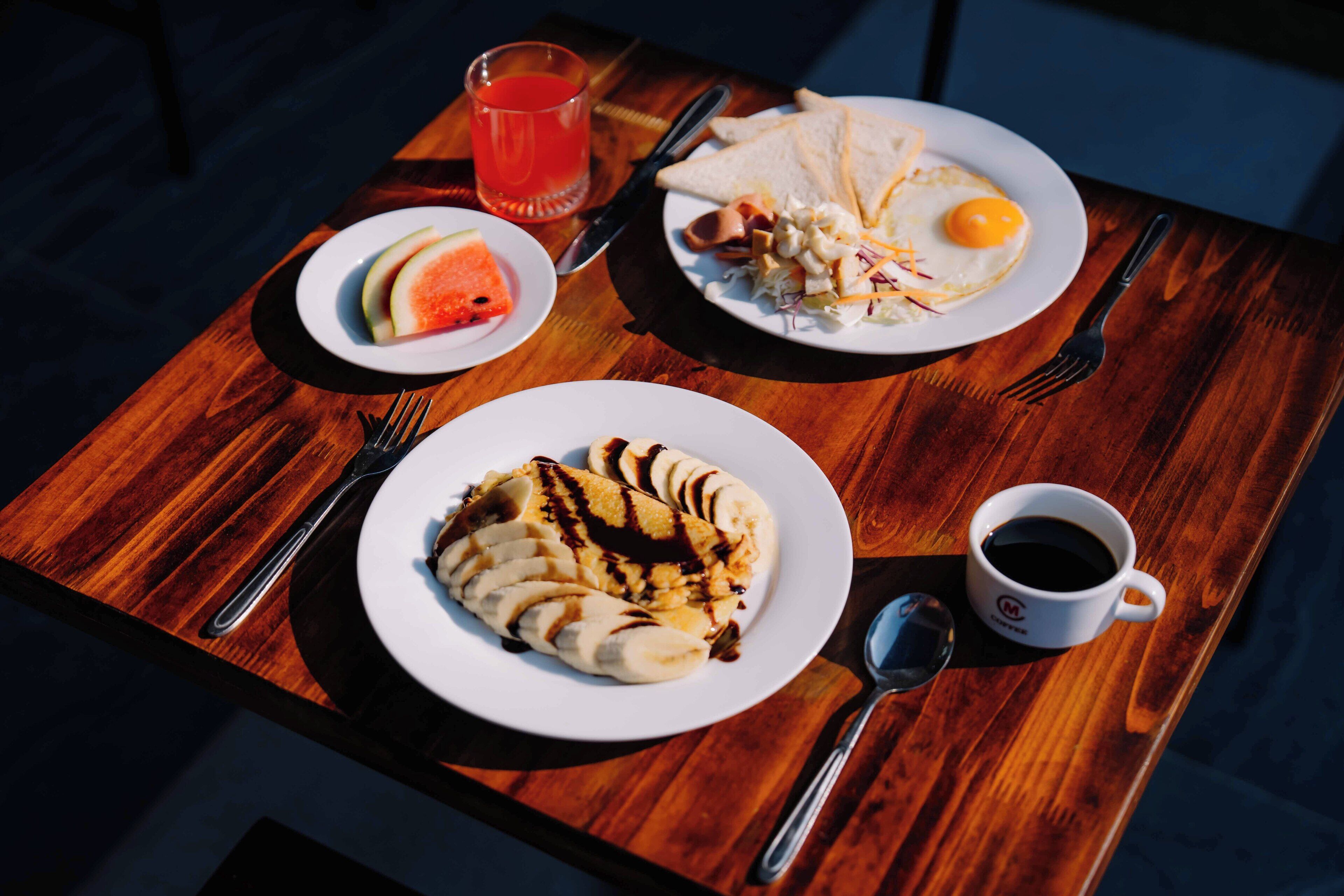 A wooden table with breakfast items including toast, eggs, and a banana split.