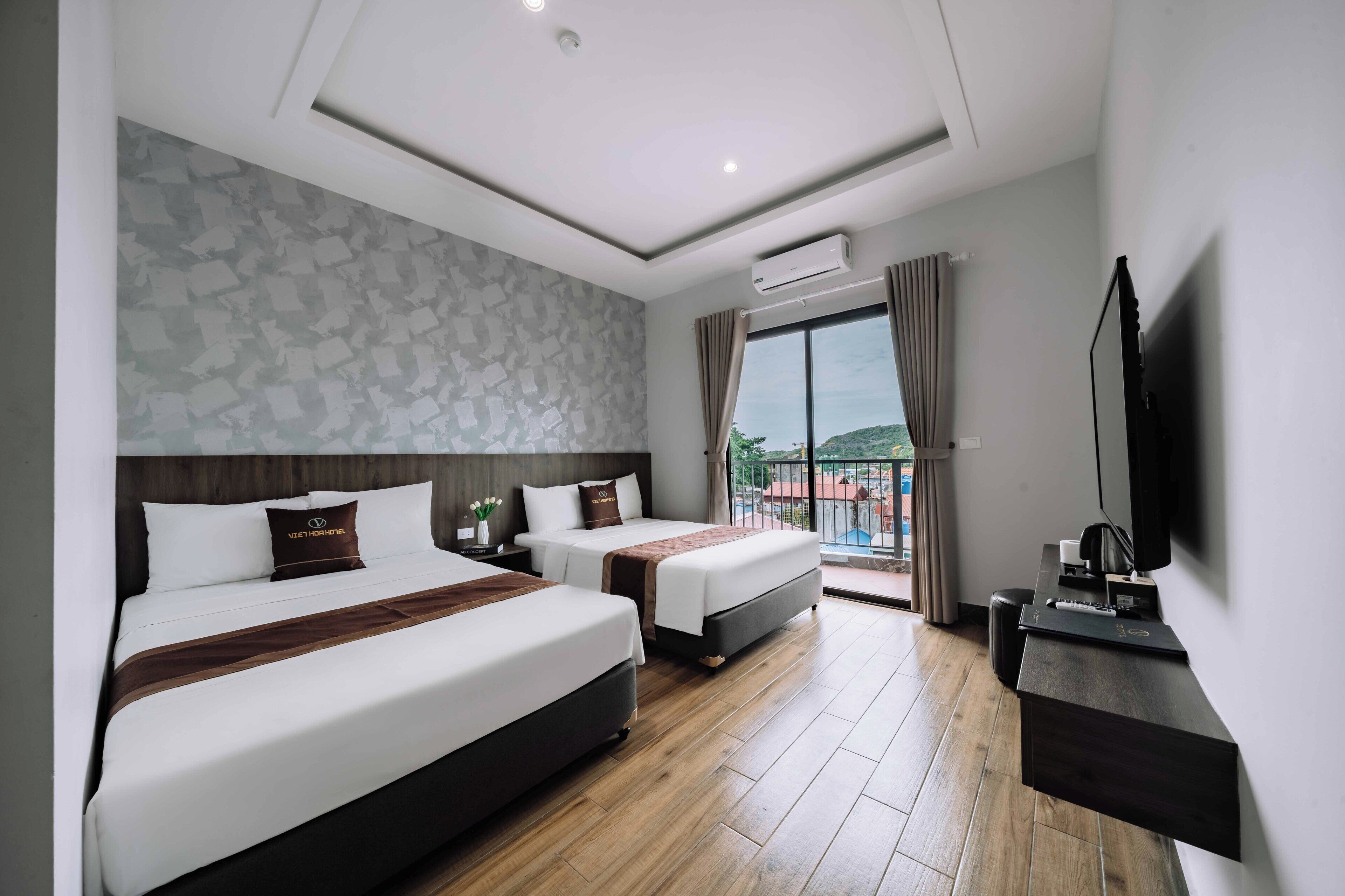 A hotel room with two beds, a flat-screen TV, a desk, and a balcony with a view.