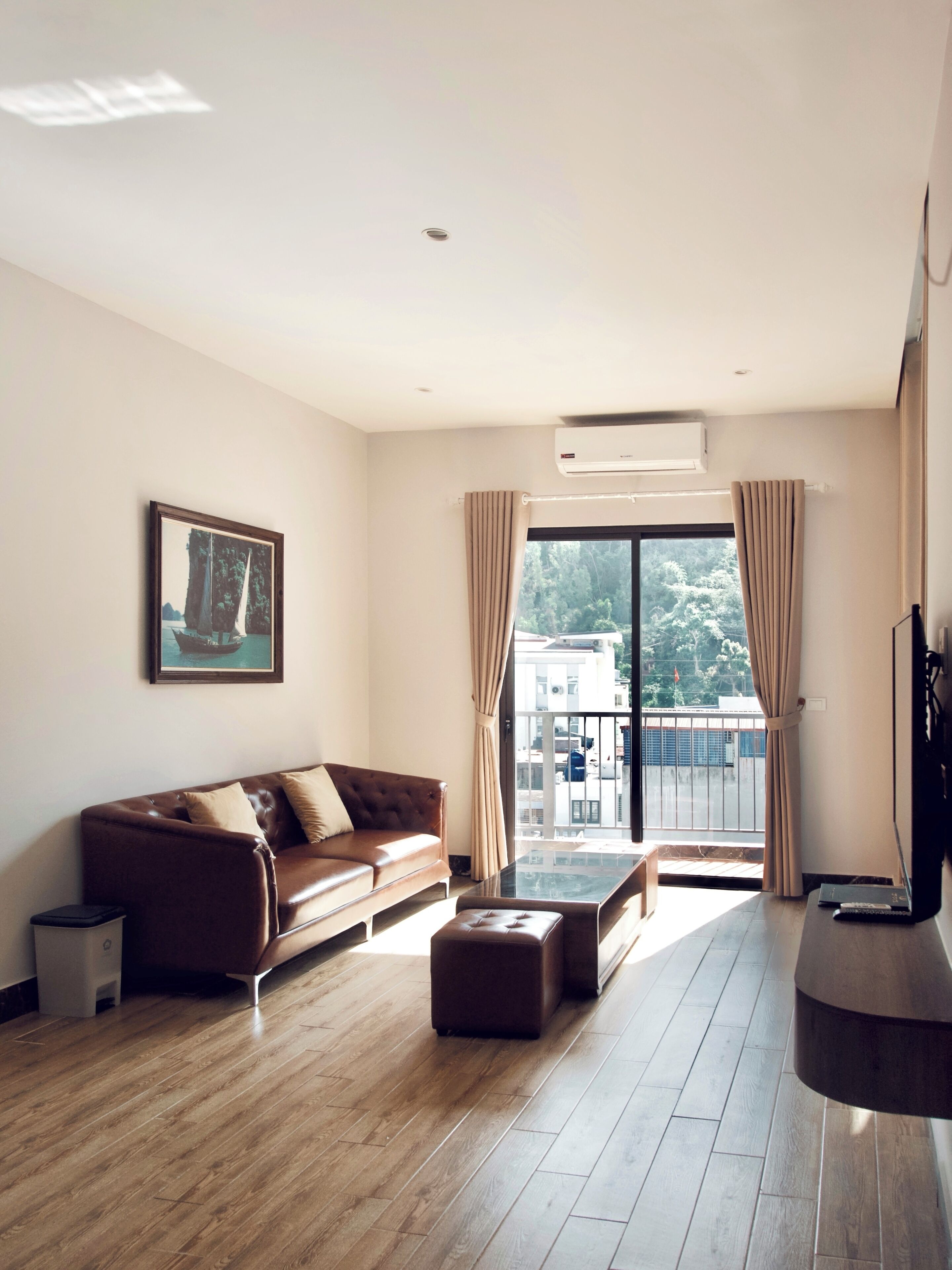 A modern living room with a leather sofa, a glass coffee table, and a view of a balcony with a railing.