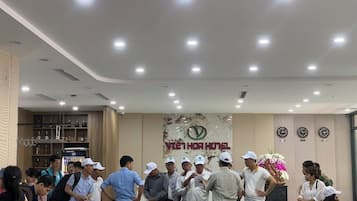 A group of people in a hotel lobby with a reception desk, a clock, and a wall with the hotel's name.