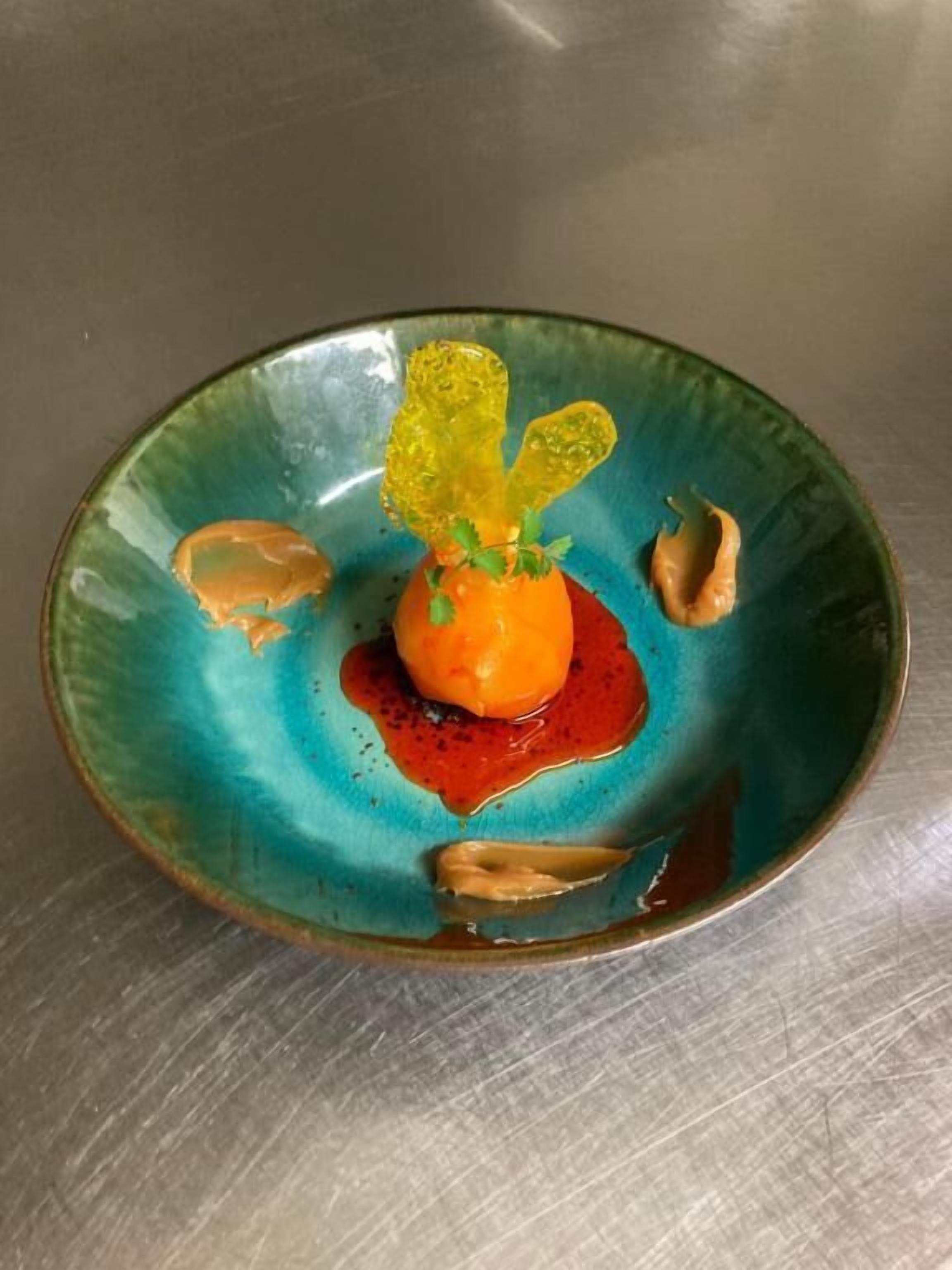 A plate with a central orange sphere, surrounded by a blue-green sauce and garnishes.