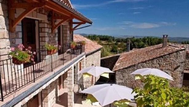 Un bâtiment en pierre doté d’un balcon, d’un espace extérieur aménagé pour s’asseoir et de parasols.