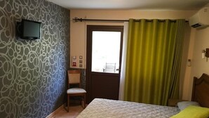 Une chambre à coucher avec un lit, une chaise, un téléviseur fixé au mur et une fenêtre avec des rideaux.