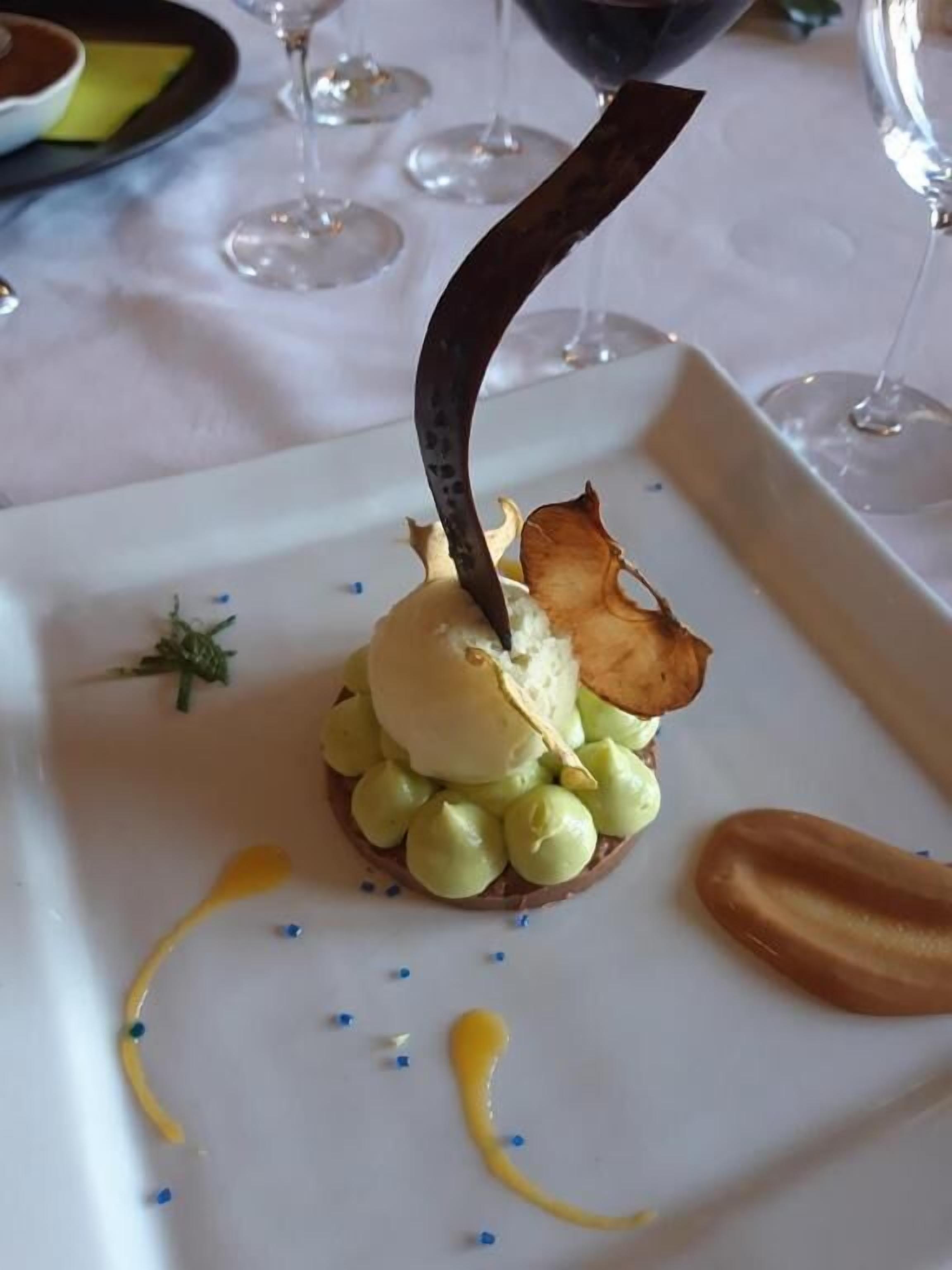 Un postre sobre un plato blanco con un adorno, rodeado de pequeños puntos azules y amarillos.
