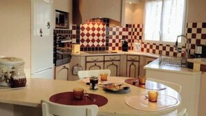 A compact kitchen with a checkered backsplash, a dining area with a round table, and a window providing natural light. - Villa la Patachou à 2 pas du Village de Malaucène (Malaucène)