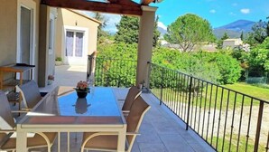 A covered patio with a table and chairs, a view of a mountain, and a well-maintained garden. - Villa la Patachou à 2 pas du Village de Malaucène (Malaucène)