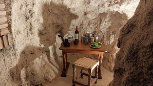 Une pièce rustique aux murs de pierre, avec une table en bois dressée pour le repas, agrémentée d’une bouteille, de verres et d’un bol de raisins.