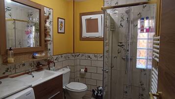Un baño con una pared amarilla, un lavabo blanco, un inodoro, una ducha con puerta de cristal y una lavadora.