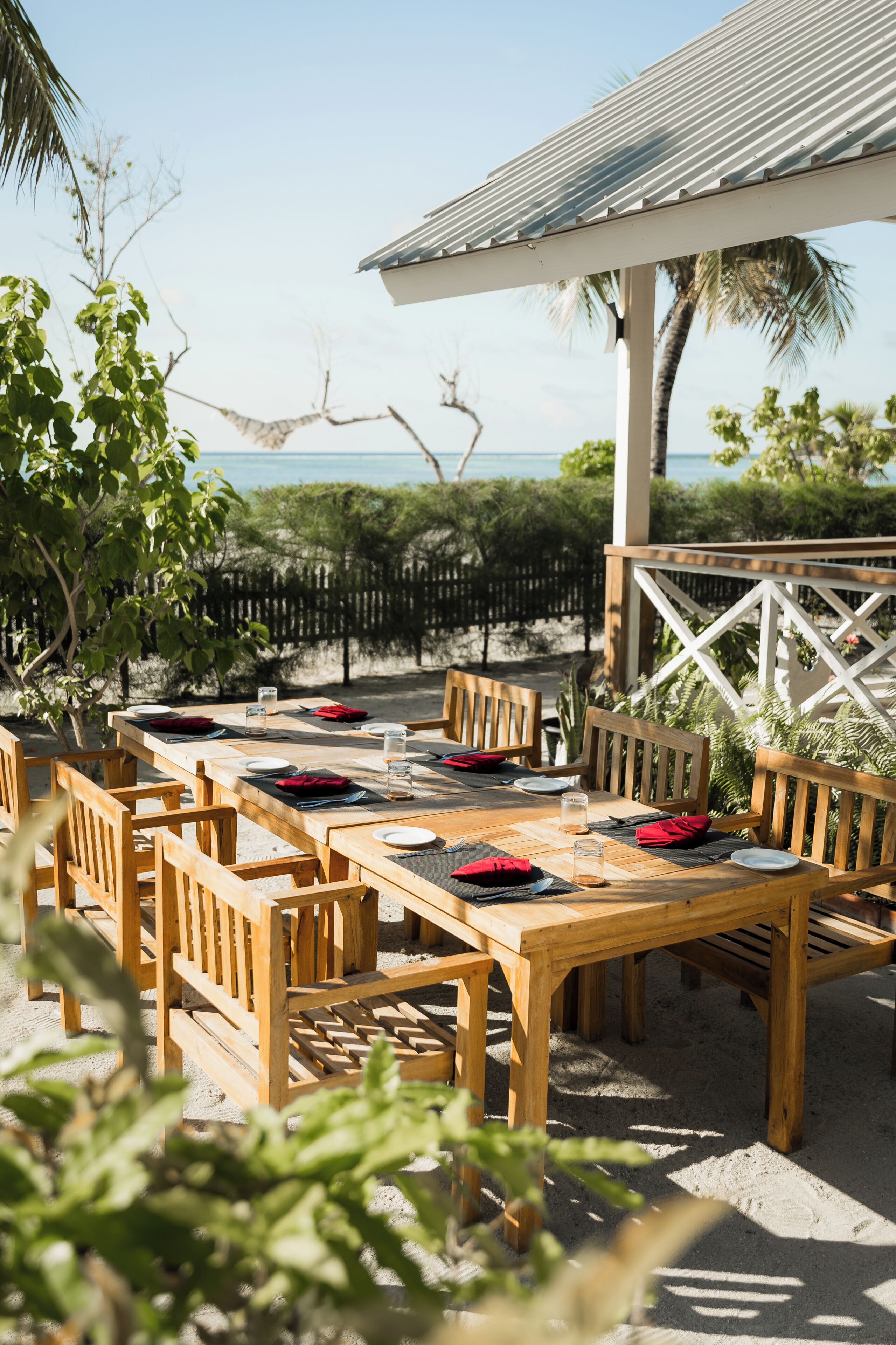 Un espace de restauration en plein air avec des tables et des chaises en bois, un coin salon abrité et une vue sur l’océan.