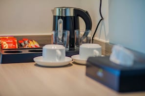 Een koffiehoek met een koffiezetapparaat, twee kopjes en een theezakjesdoos.