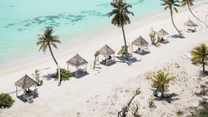 Une plage avec une eau turquoise et limpide, des palmiers et des cabanes de plage.