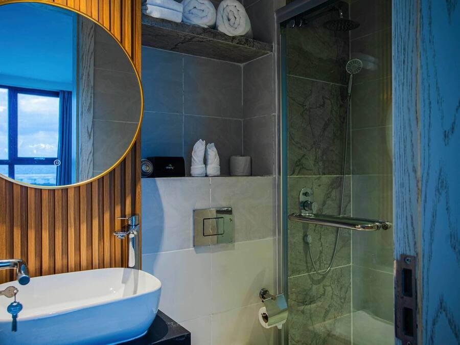 Un bagno con un lavandino bianco, uno specchio, una doccia con porta in vetro e un portasciugamani con asciugamani.