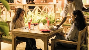 Un espace extérieur aménagé pour les repas, avec des tables et des chaises en bois, entouré de verdure.
