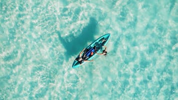 Vista aérea de un mar turquesa cristalino con una persona sobre una tabla de surf azul.
