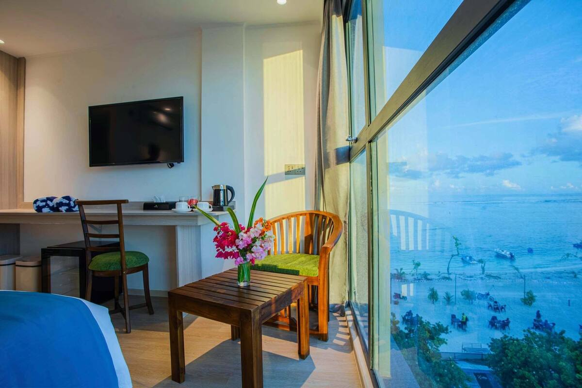 Een hotelkamer met een groot raam, een bed, een bureau met een flatscreen televisie, een houten tafel en twee stoelen.
