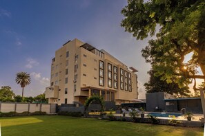 A modern multi-story building with a flat roof, large windows, and a swimming pool area with lounge chairs. - VEGA by The Ozone Hotel Udaipur (Udaipur)