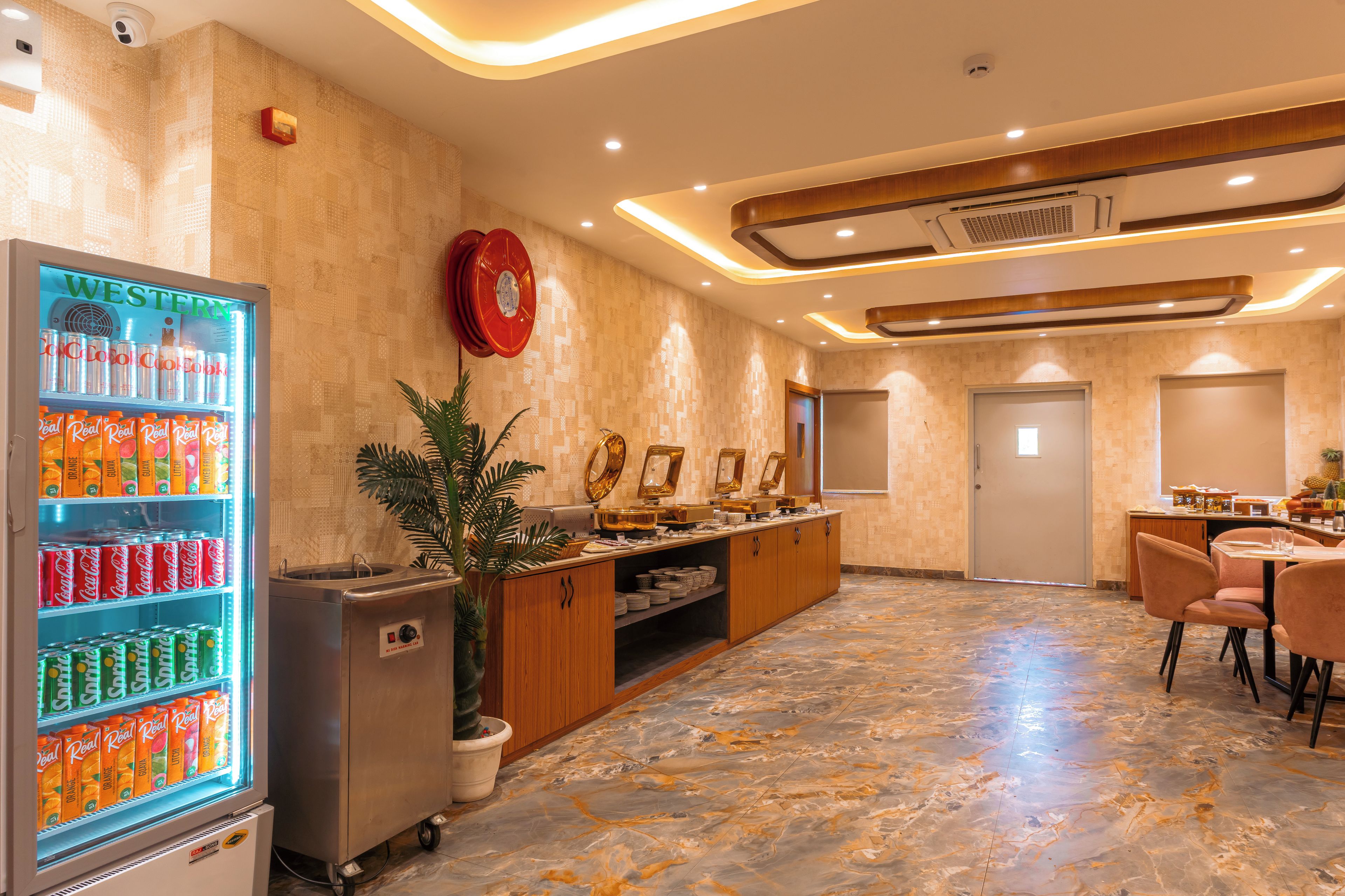A hotel lobby with a self-service beverage station, a buffet area, and a seating area with tables and chairs.