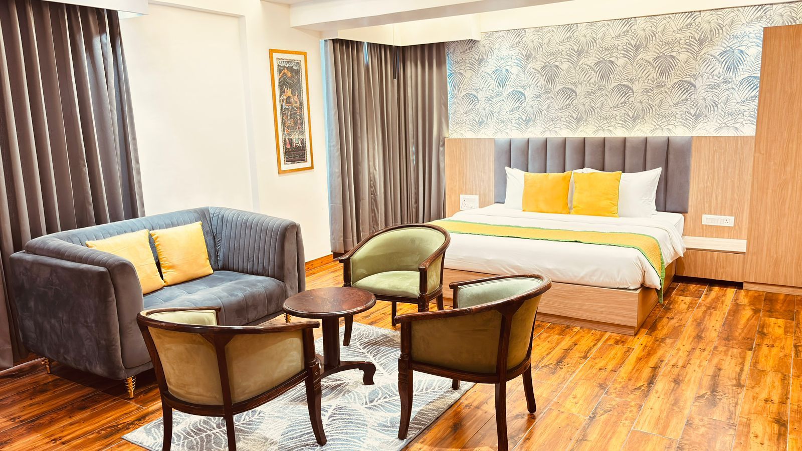 Habitación de hotel con cama, sofá, dos sillones, una mesita y una alfombra estampada.