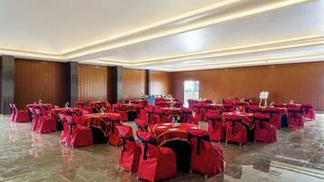 A large hall with rows of tables and chairs, each set covered with red tablecloths and matching chair covers.