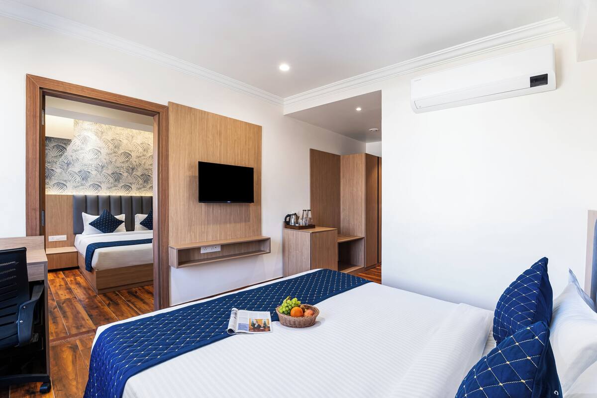 A modern hotel room with a large bed, a flat-screen TV, a wooden wardrobe, and a small seating area.