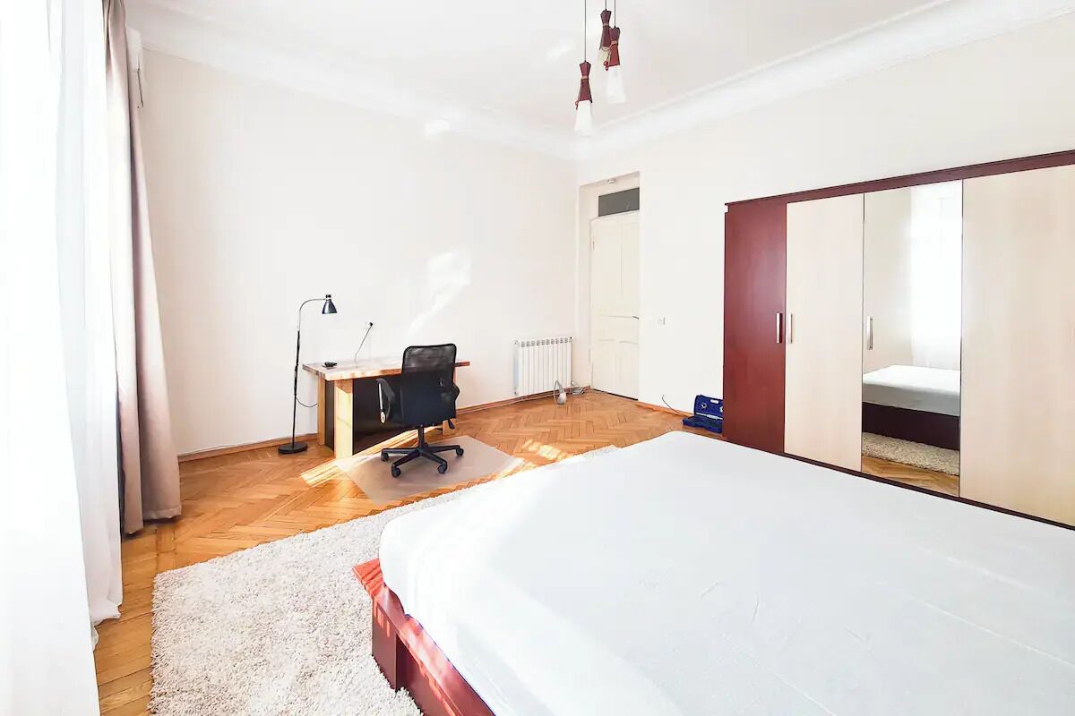 Ein Schlafzimmer mit einem großen Bett, einem Schreibtisch mit Stuhl, einem Heizkörper und einem Kleiderschrank.