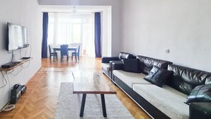 Un salon moderne avec un canapé en cuir, une table basse en bois et un téléviseur fixé au mur.