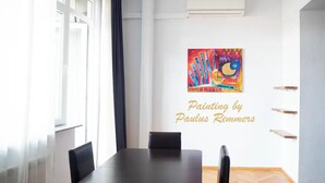 Un coin repas avec une table et des chaises, un tableau accroché au mur et une fenêtre avec des rideaux.