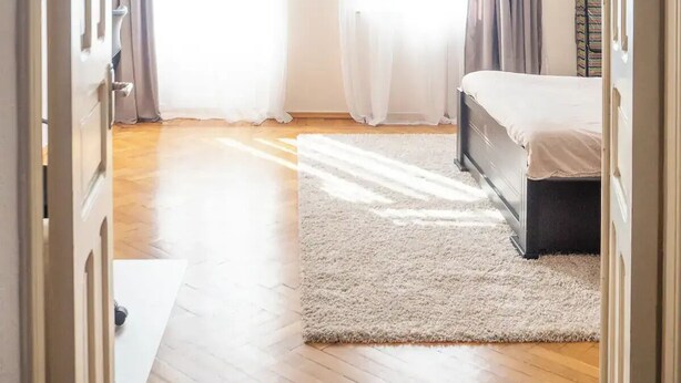 Une chambre à coucher comprenant un lit, une table de chevet, une commode, une grande fenêtre avec des rideaux et un ventilateur de plafond.