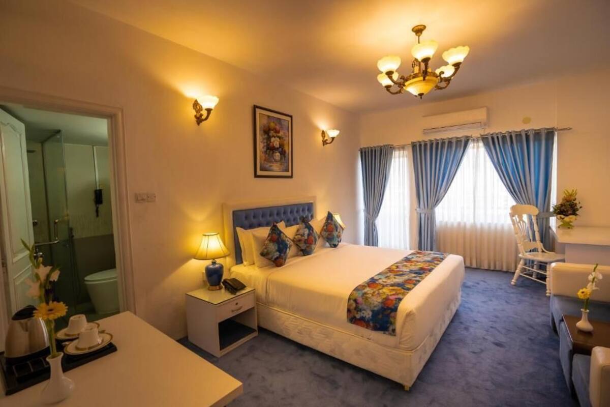 Ein Hotelzimmer mit einem großen Bett, Nachttischen, einem Schreibtisch, einem Sessel und einer Dusche.